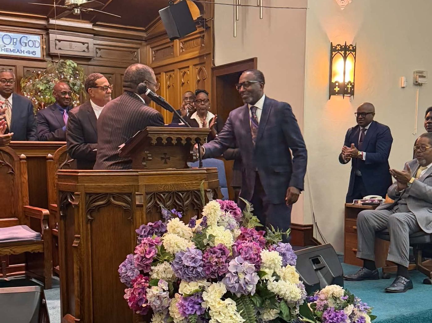 Pastor Hughes shaking hands at the pulpit as ministers applaud